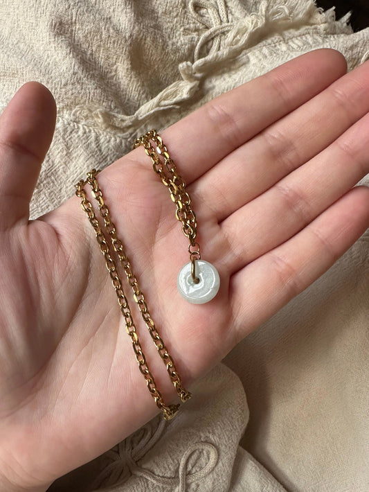 Gold chain with a jade pendant held in a hand on a textured fabric background