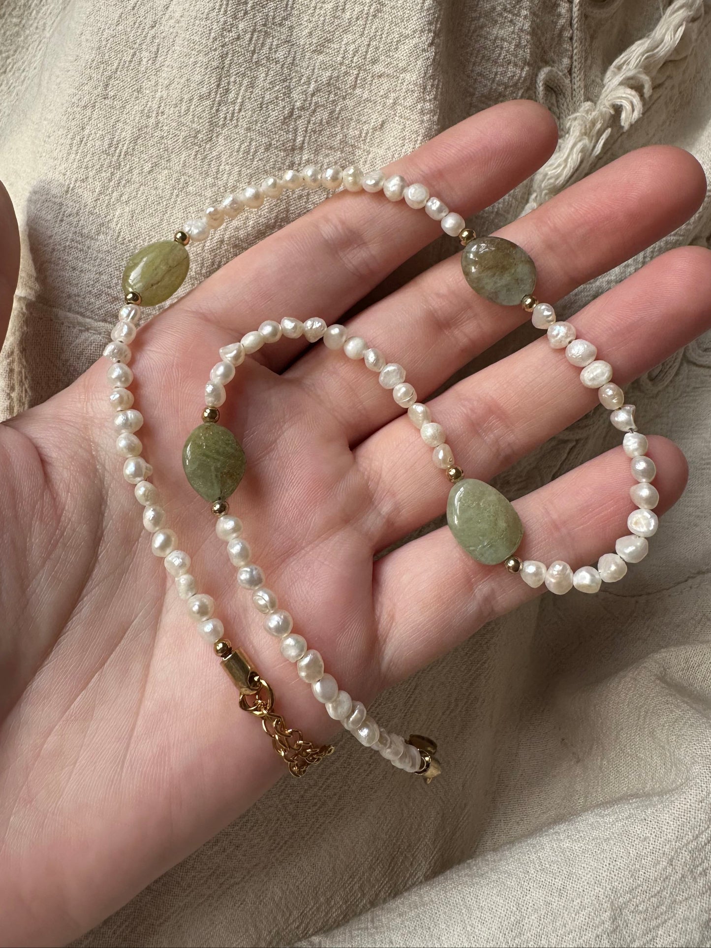 Hand holding a pearl necklace with gold accents on a neutral fabric background