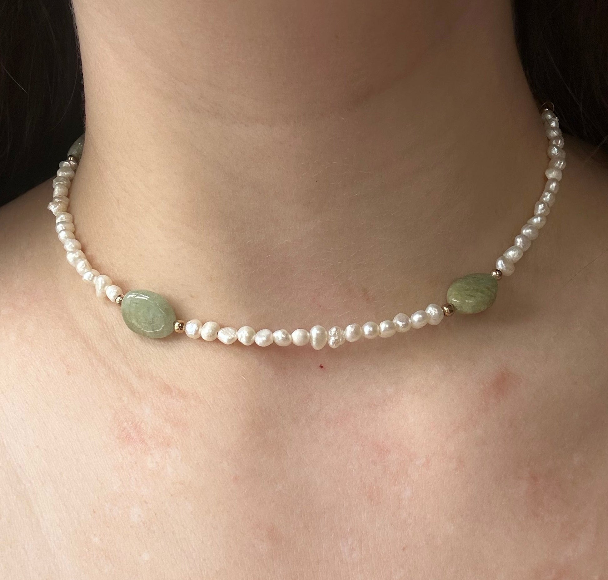 Close-up of a pearl necklace with green beads on a person's neck.