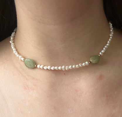 Close-up of a pearl necklace with green beads on a person's neck.