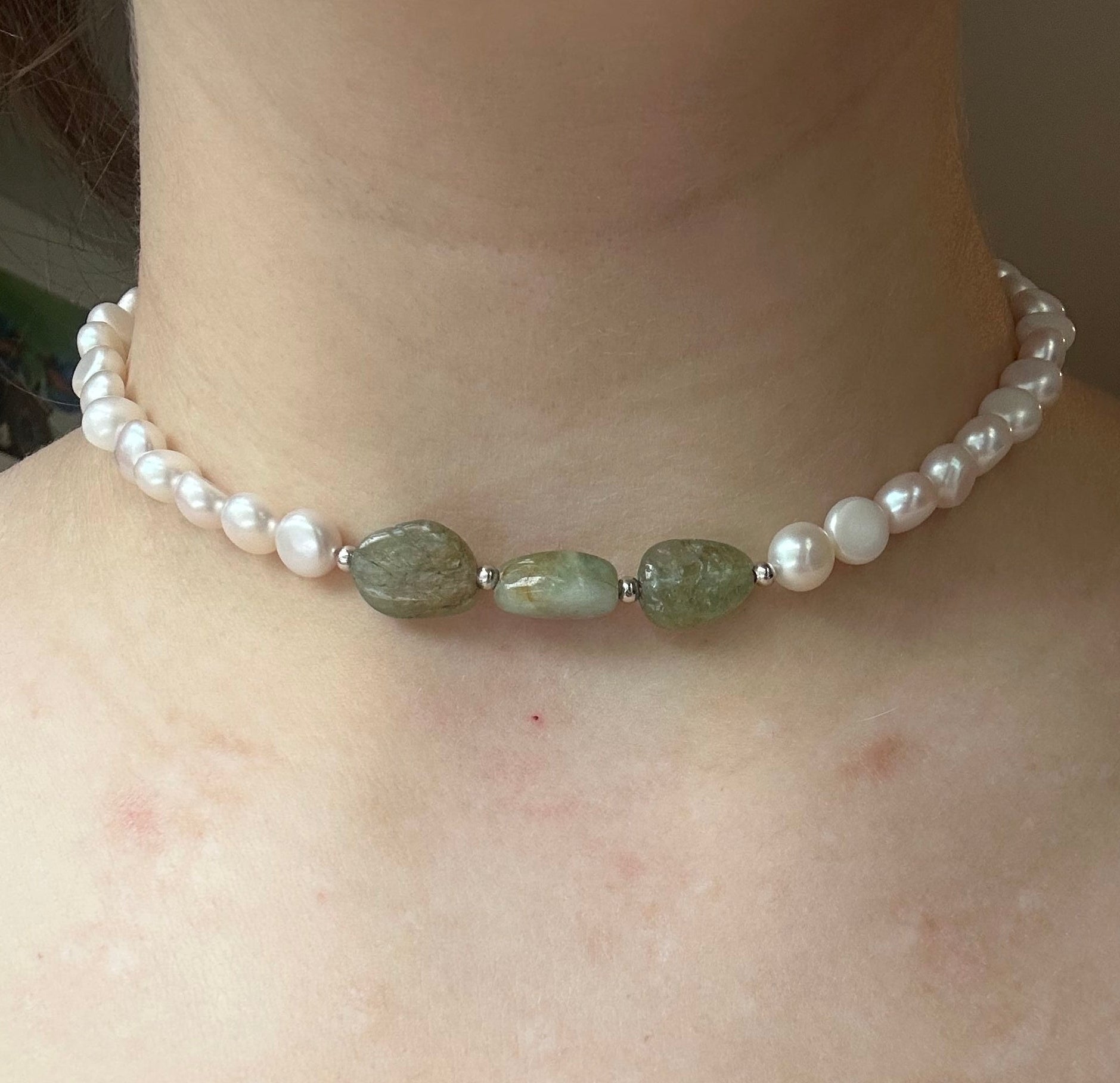 Pearl and green stone necklace on a person's neck with a neutral background