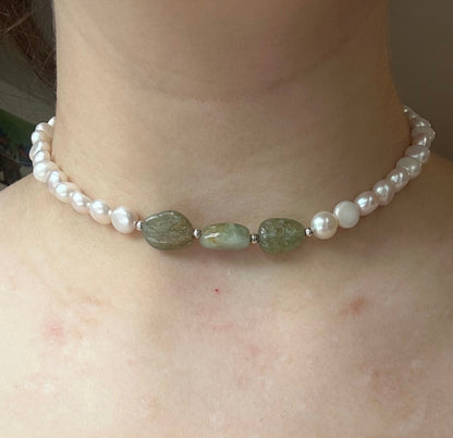Pearl and green stone necklace on a person's neck with a neutral background