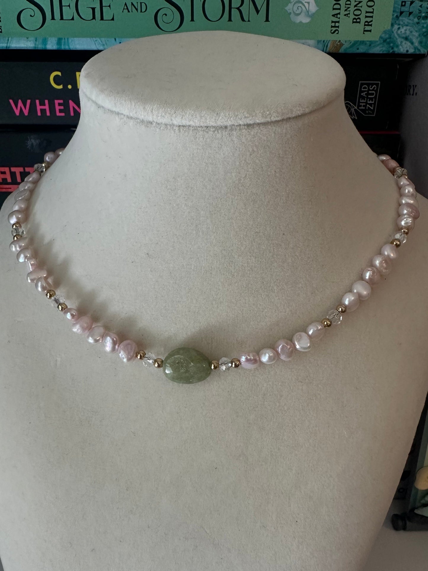 Pearl necklace with a green stone on a mannequin bust against a bookshelf background
