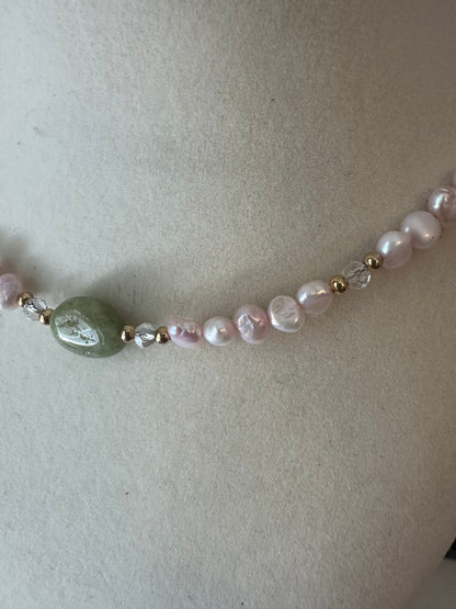 Necklace with pearls and a green bead on a light background